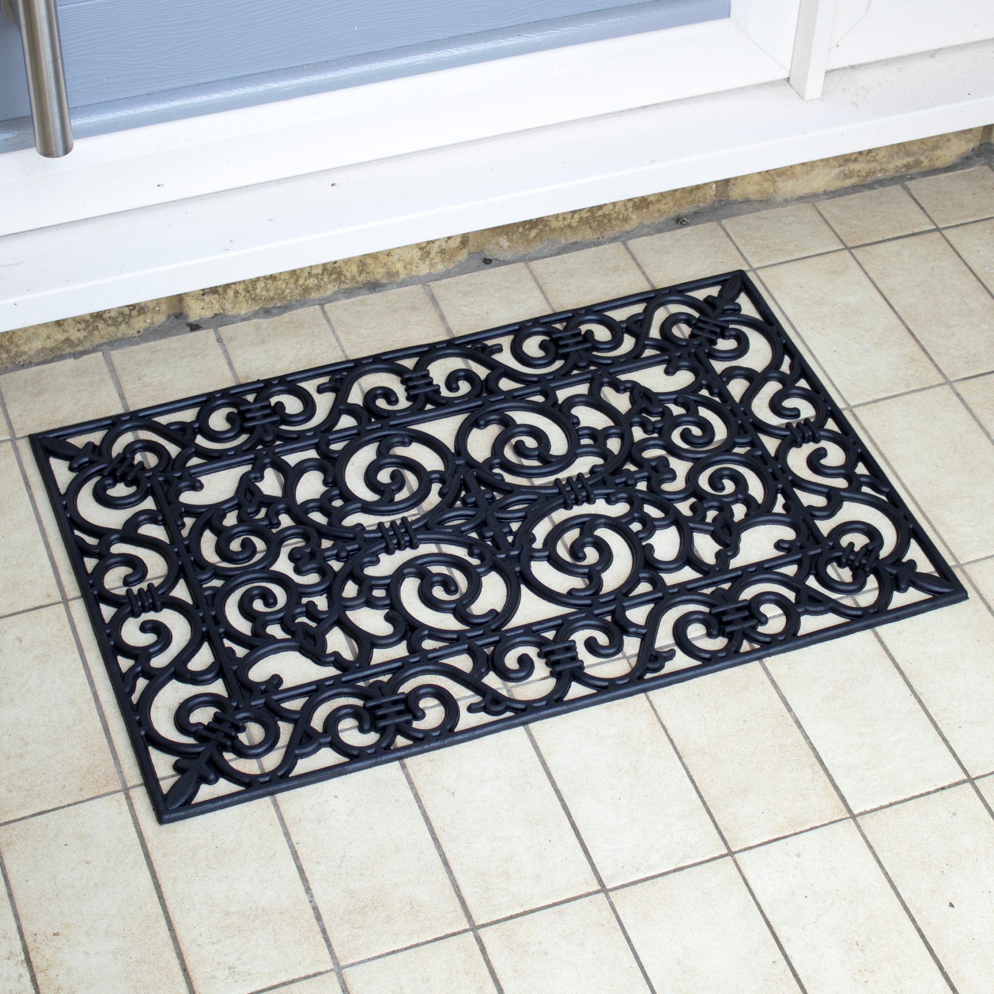 Decorative black rubber doormat with intricate patterns on a tiled floor.