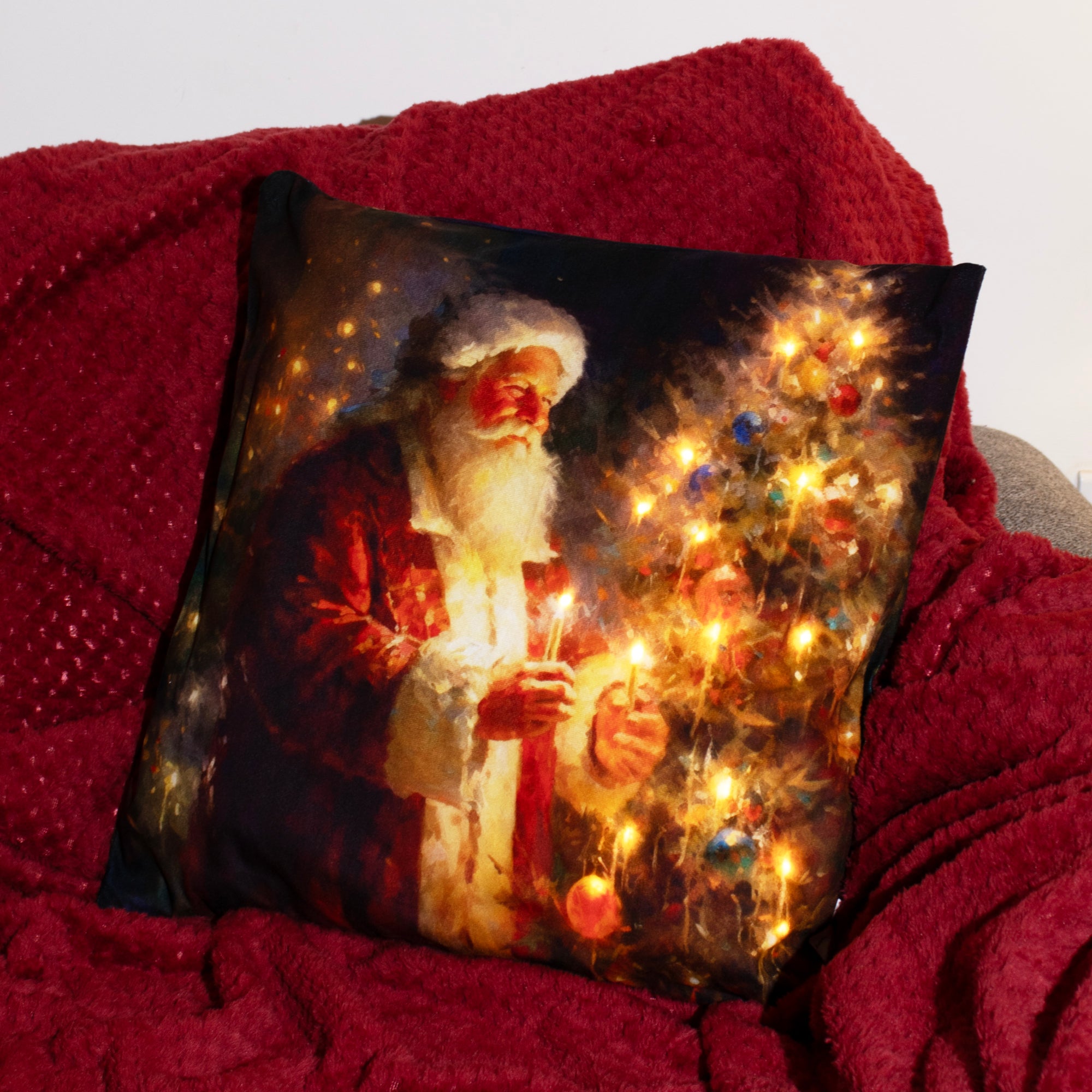 An LED cushion featuring a festive scene with Santa Claus, a Christmas tree, and candles, placed on a cozy, red textured surface.