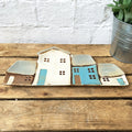 A ceramic plate featuring a row of four house designs in beige, blue, and brown colors on a wooden surface.