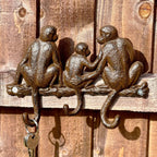 Wall-mounted cast iron hooks with a design featuring three monkeys sitting and facing forward.