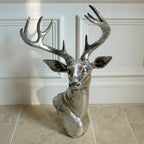 A silver-colored wall-mounted sculpture of a stags head with large antlers, placed against an indoor background.