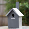 Grey birdhouse with a silver roof on a blurred natural background