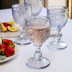 A set of four blue embossed glass wine goblets on a table with food in the background, displayed as a gift set.