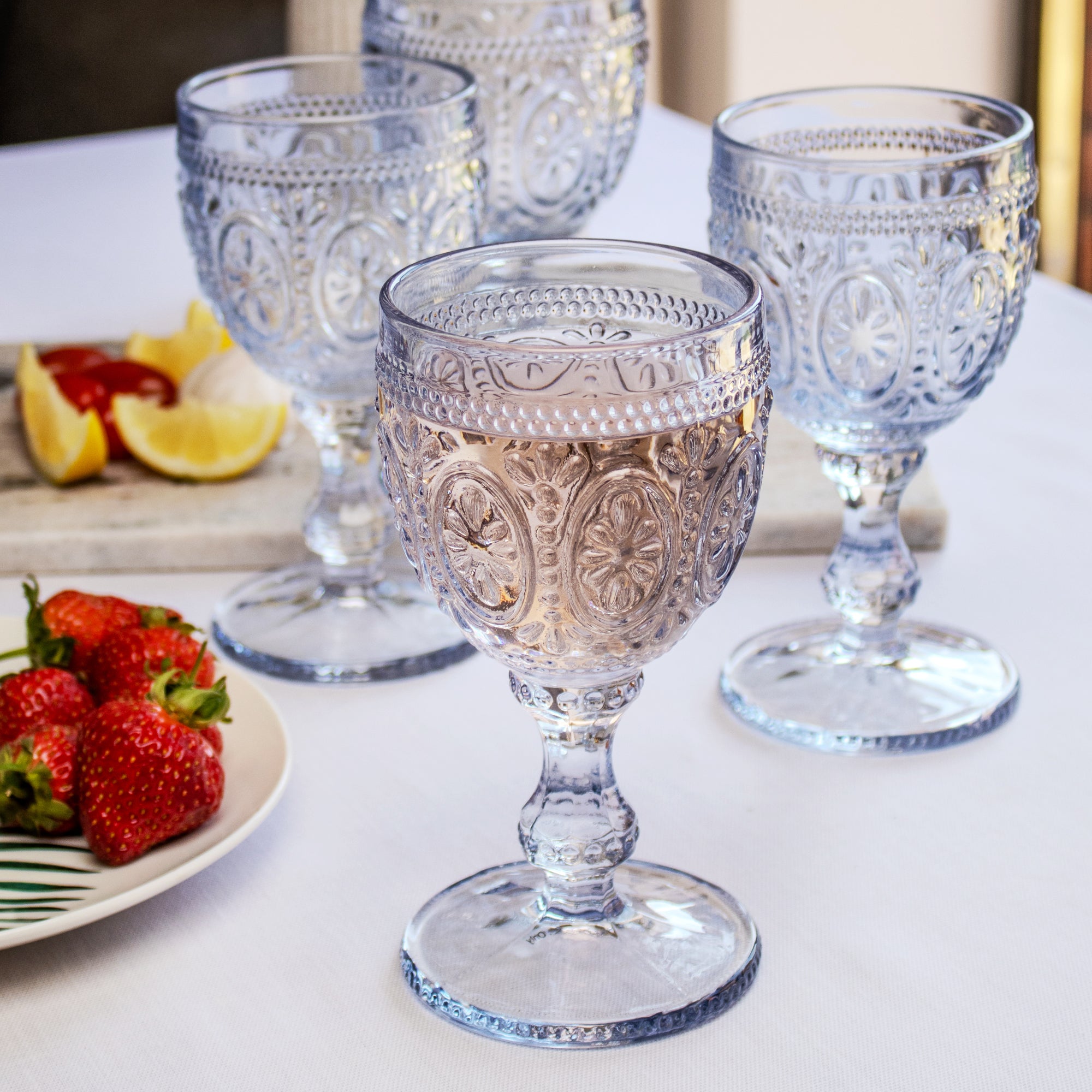 A set of four blue embossed glass wine goblets on a table with food in the background, displayed as a gift set.