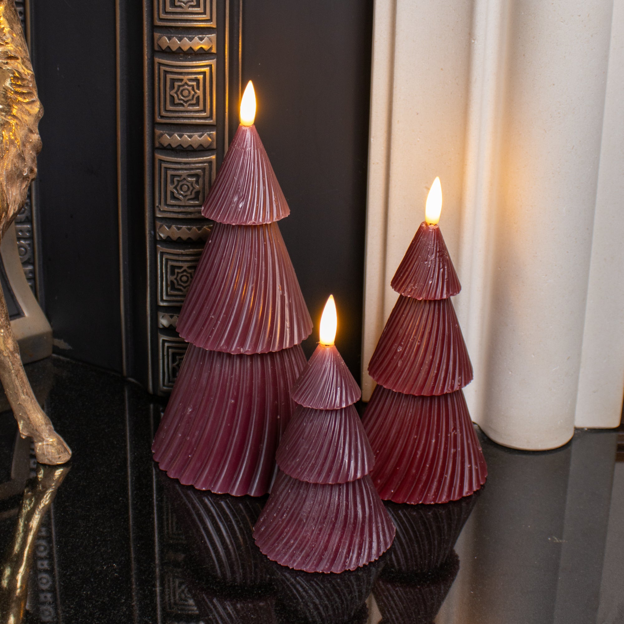 A set of three wine red LED candles designed to resemble Christmas trees, displayed indoors with a warm glow from the LEDs.