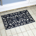 Decorative black rubber doormat with intricate patterns on a tiled floor.