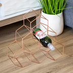 Geometric copper wine rack holding a bottle on a wooden surface with a plant in the background.