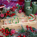 Set of four glass serving bowls with Christmas-themed designs, placed on a bamboo wooden sleigh-shaped tray, surrounded by festive decorations like pine cones, holly, and Christmas tree branches.