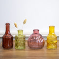 Four citrus coloured glass vases on a wooden surface with a white wall background.