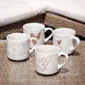 Set of four white mugs with heart designs on a woven surface