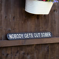 Black decorative garden sign that says "NOBODY GETS OUT SOBER" in white block text