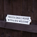 Decorative sign with text 'This is a small house with a big welcome' on a wooden background