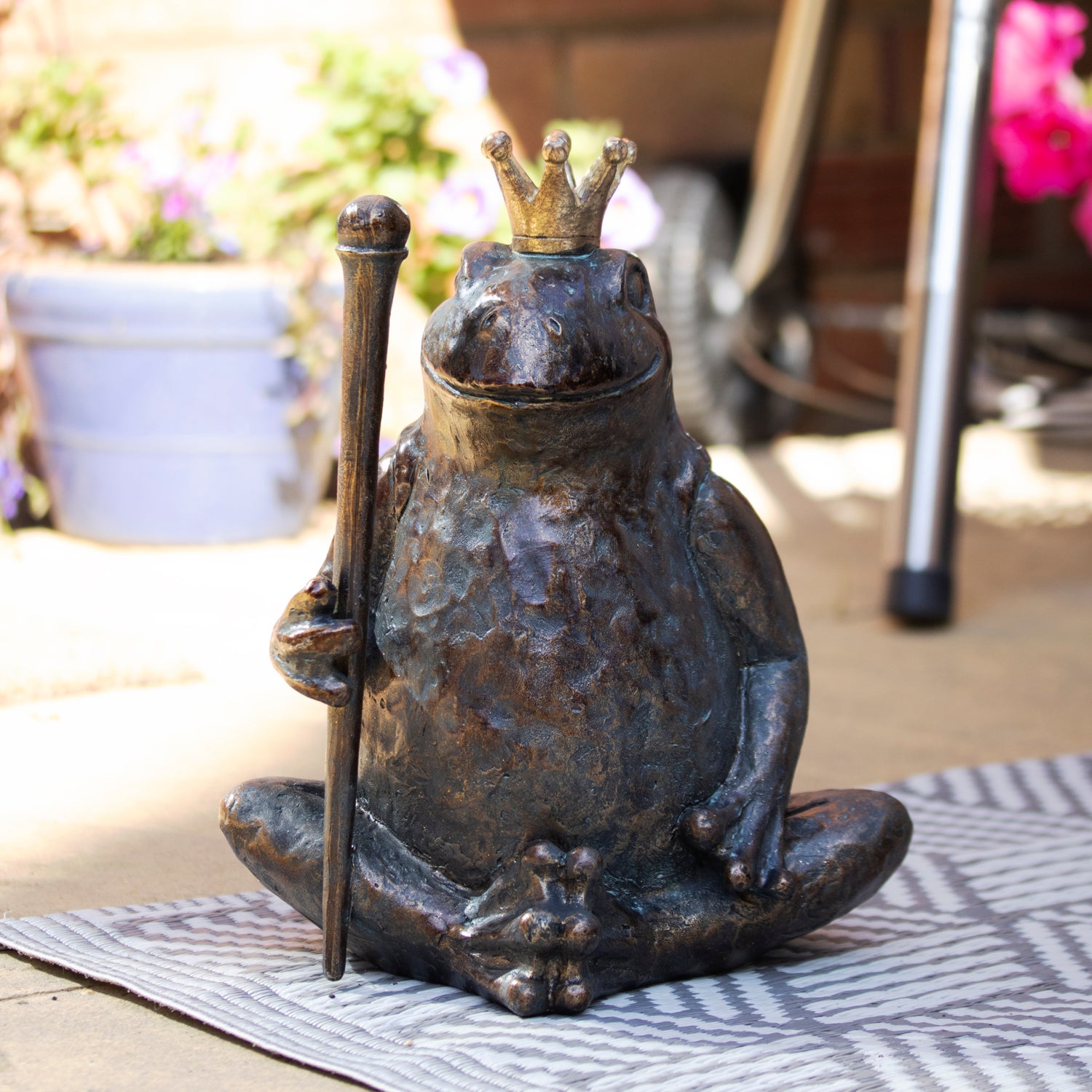 Bronze frog statue with a gold royal crown and scepter on a garden patio setting