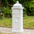 Decorative white post box with intricate designs on a grassy background