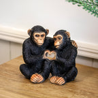 Two monkey figurines holding a heart-shaped object on a wooden surface.
