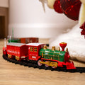 A red and green toy train set with a Christmas tree ornament in the background, set up on a wooden floor.