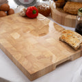 A large end grain chopping board made of rubber wood with molded handles, displayed with food items around it.