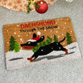 A Christmas-themed doormat featuring a black dachshund running through snow, with festive decorations such as Christmas trees and snowflakes, and the text 'DACHSHUND Through THE SNOW'.
