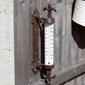 A wall-mounted cast iron thermometer with a Fleur-de-Lis design, displaying temperatures in Celsius.