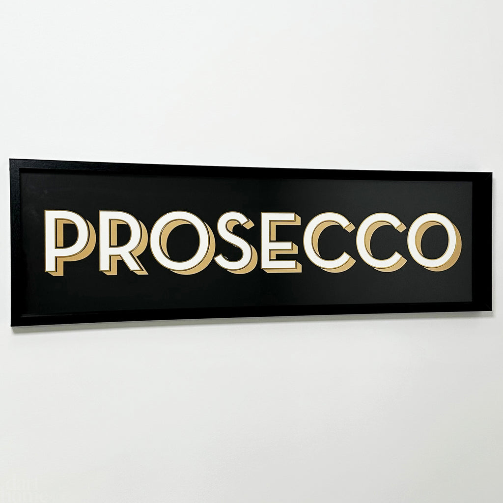 A black framed wall mounted 'Prosecco' bar sign with block typography and a 3D effect, featuring white and gold letters on a black background.