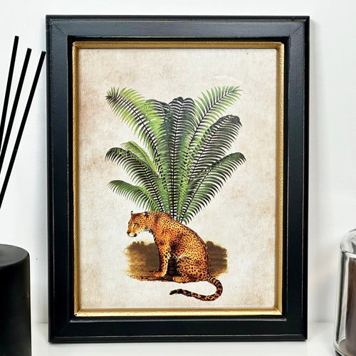 A toile framed print depicting a leopard in a jungle setting with a black frame and gold trim.