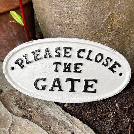 Weißes Gusseisen-Schild „Bitte schließen Sie das Tor“.